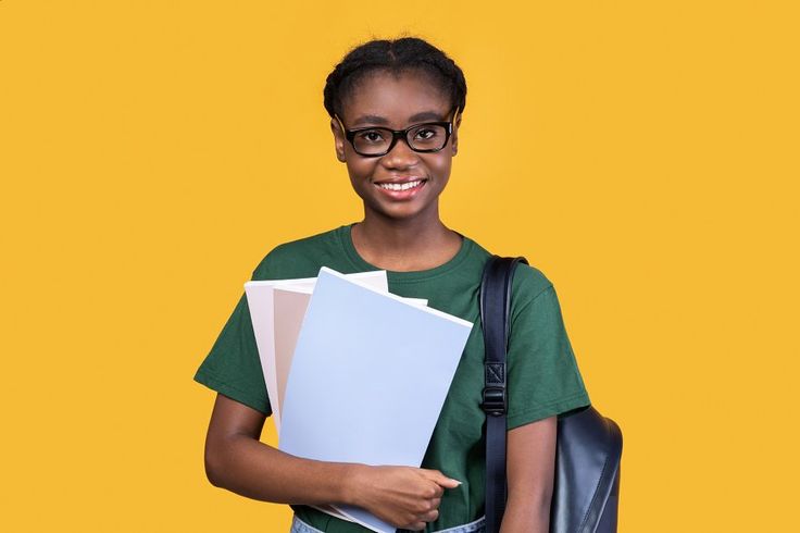 happy black female student posing with books on yellow background