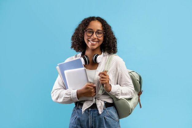 online education smiling black female student with backpack and headphones holding notebooks and premium photo